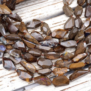 May include: A strand of brown, gold, and blue opal gemstone beads. The beads are faceted and have a rough, natural look. They are strung on a red thread.