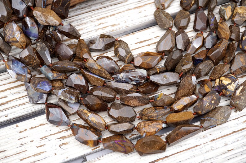 May include: A strand of brown, gold, and blue opal gemstone beads. The beads are faceted and have a rough, natural look. They are strung on a red thread.
