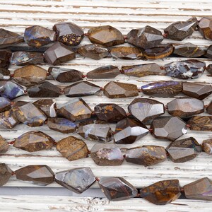 May include: A strand of brown and iridescent opal gemstone beads, faceted and shaped into irregular, elongated ovals. The beads are strung on a thin wire and are arranged in a loose, flowing pattern.