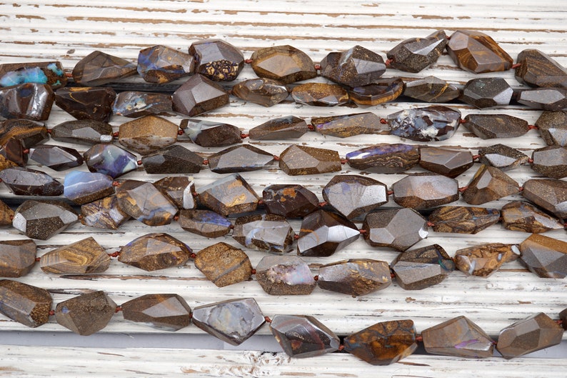 May include: A strand of brown and iridescent opal gemstone beads, faceted and shaped into irregular, elongated ovals. The beads are strung on a thin wire and are arranged in a loose, flowing pattern.