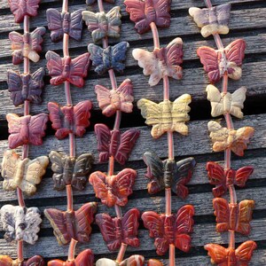 May include: A strand of gemstone butterfly beads in various shades of red, brown, white, and black. The beads are strung on a clear elastic cord.