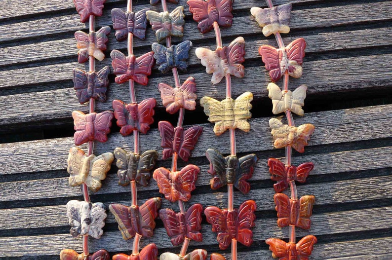 May include: A strand of gemstone butterfly beads in various shades of red, brown, white, and black. The beads are strung on a clear elastic cord.