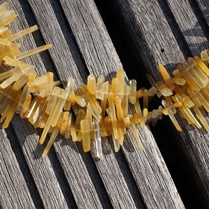 May include: A necklace made of many small, light brown, clear quartz crystal points. The necklace is laid out on a wooden surface.