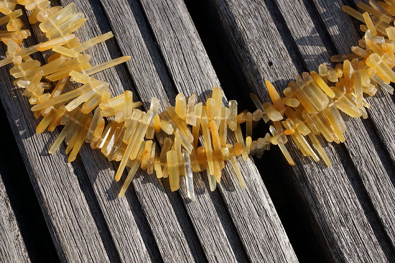May include: A necklace made of many small, light brown, clear quartz crystal points. The necklace is laid out on a wooden surface.