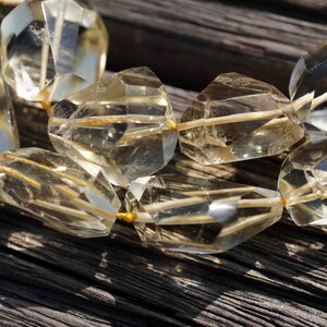 May include: A strand of faceted, clear, light yellow gemstone beads. The beads are strung on a thin, gold thread. The beads are arranged in a random pattern.