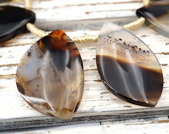 May include: A strand of brown and black agate gemstone beads with a gold cord. The beads are in the shape of teardrops.