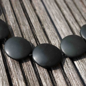 May include: A black necklace made of round, smooth stones connected by black string. The necklace is lying on a wooden surface.