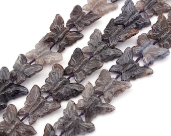 May include: A strand of gray and purple gemstone butterfly beads. The beads are carved in the shape of butterflies and are strung on a purple cord.