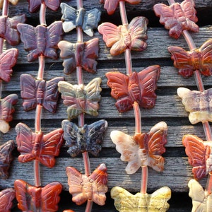 May include: A strand of gemstone butterfly beads in shades of red, brown, and white. The beads are strung on clear elastic cord.