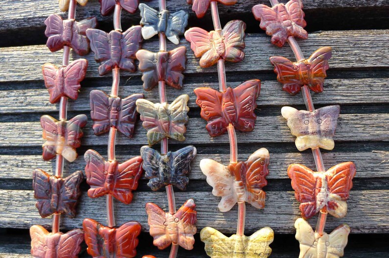 May include: A strand of gemstone butterfly beads in shades of red, brown, and white. The beads are strung on clear elastic cord.