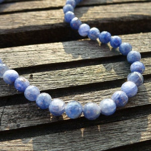 May include: A necklace made of blue gemstone beads. The beads are round and have a slightly irregular shape. The necklace is lying on a wooden surface.
