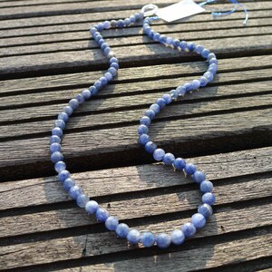 May include: A blue gemstone bead necklace on a wooden surface. The necklace is made of round beads and has a silver clasp.