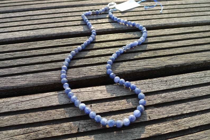 May include: A blue gemstone bead necklace on a wooden surface. The necklace is made of round beads and has a silver clasp.