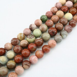May include: A strand of round, multi-colored gemstone beads. The beads are a mix of brown, red, pink, and green shades. The beads are all about 1 cm in diameter.