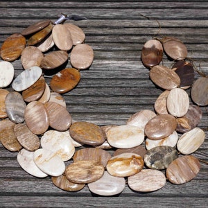Puede incluir: Un collar hecho de cuentas de madera petrificada de forma ovalada en tonos marrones, beige y blancos. Las cuentas est&aacute;n dispuestas en una doble hilera y est&aacute;n enhebradas en un cord&oacute;n marr&oacute;n.