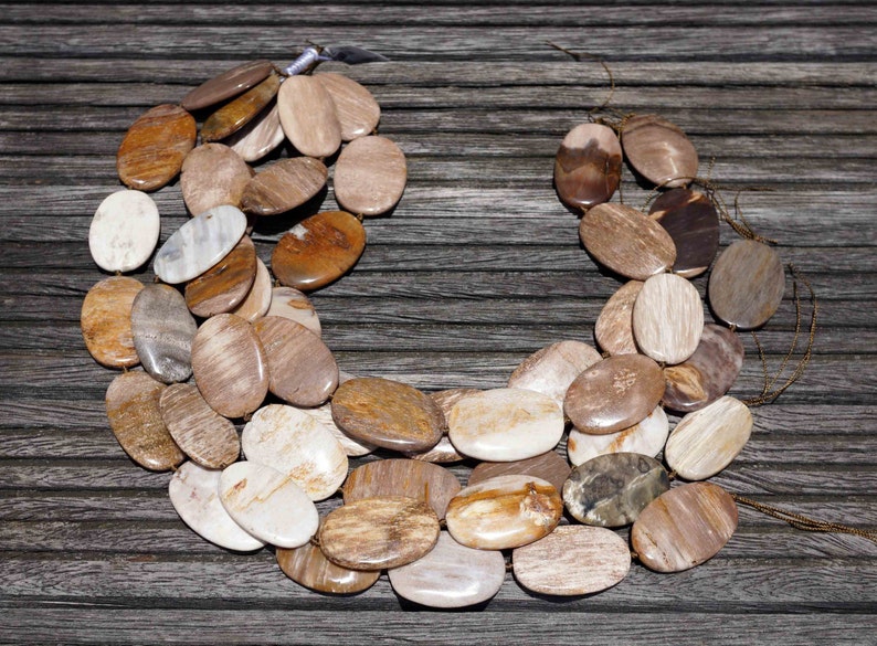 Puede incluir: Un collar hecho de cuentas de madera petrificada de forma ovalada en tonos marrones, beige y blancos. Las cuentas est&aacute;n dispuestas en una doble hilera y est&aacute;n enhebradas en un cord&oacute;n marr&oacute;n.