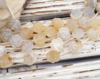 May include: A strand of white and beige agate rose beads. The beads are carved in the shape of roses and are strung on a white cord.