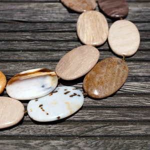 Puede incluir: Primer plano de un collar hecho de piedras ovaladas en tonos marrones, blancos y beige. Las piedras est&aacute;n enhebradas con un cord&oacute;n fino y est&aacute;n dispuestas en un patr&oacute;n.