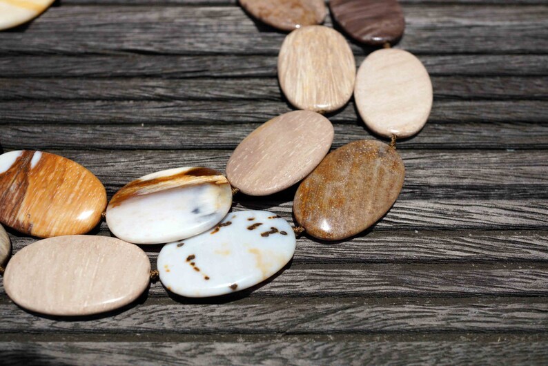 Puede incluir: Primer plano de un collar hecho de piedras ovaladas en tonos marrones, blancos y beige. Las piedras est&aacute;n enhebradas con un cord&oacute;n fino y est&aacute;n dispuestas en un patr&oacute;n.