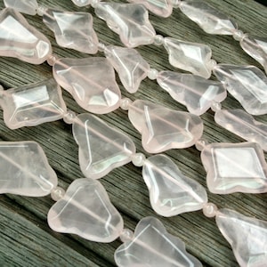 May include: A strand of pink rose quartz beads, each bead is faceted and has a unique shape. The beads are strung on a clear elastic cord.