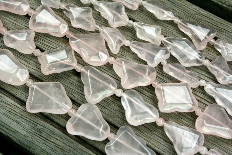 May include: A strand of pink rose quartz beads, each bead is faceted and has a unique shape. The beads are strung on a clear elastic cord.