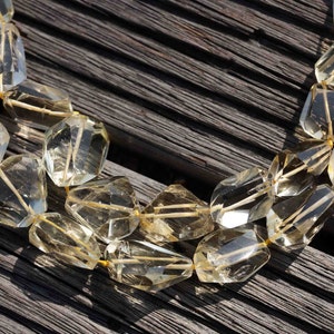 May include: A strand of light yellow faceted gemstone beads, strung on a gold thread, on a dark wood background.