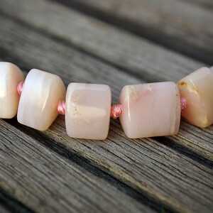 May include: A close-up of a pink opal beaded necklace with pink thread connecting the beads.
