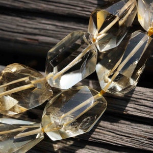 May include: A close-up of a strand of faceted, clear, and golden citrine gemstone beads. The beads are strung on a thin, gold thread and are arranged in a staggered pattern.
