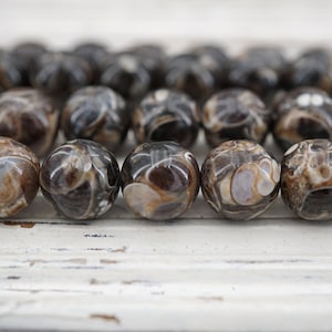 May include: A strand of brown and white agate beads with a swirling pattern. The beads are round and smooth.