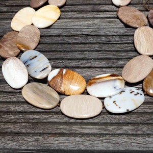 Puede incluir: Un collar hecho de piedras ovaladas pulidas en tonos marrones, blancos y beige. Las piedras tienen un aspecto natural y org&aacute;nico y est&aacute;n enhebradas con un cord&oacute;n marr&oacute;n.