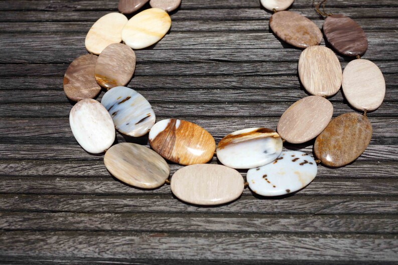 Puede incluir: Un collar hecho de piedras ovaladas pulidas en tonos marrones, blancos y beige. Las piedras tienen un aspecto natural y org&aacute;nico y est&aacute;n enhebradas con un cord&oacute;n marr&oacute;n.