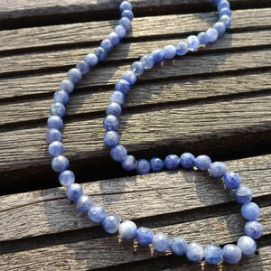 May include: A blue gemstone bead necklace on a wooden surface. The beads are round and have a slightly iridescent finish.