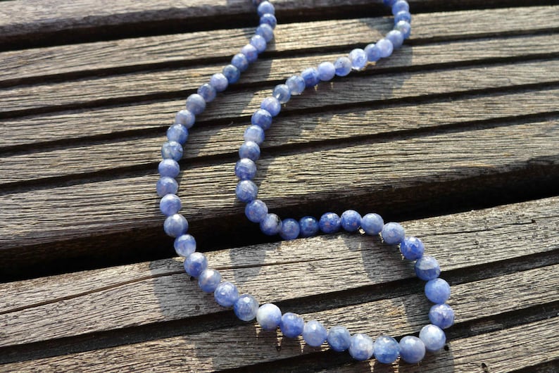 May include: A blue gemstone bead necklace on a wooden surface. The beads are round and have a slightly iridescent finish.