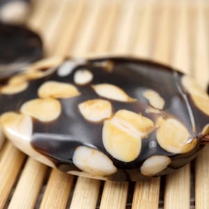May include: Close-up of a black and white patterned oval bead with a brown cord. The bead has a smooth, glossy finish and is made of natural materials.