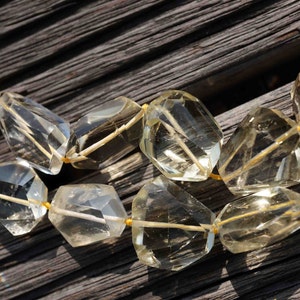 May include: A strand of clear, faceted gemstone beads with a golden yellow hue. The beads are strung on a thin, gold wire and are arranged in a staggered pattern. The beads are lying on a dark wooden surface.