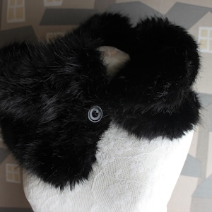 May include: A black faux fur collar with a large, round button in the centre. The collar is made of soft, fluffy fur and is perfect for adding a touch of warmth and style to any outfit.