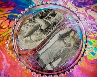 May include: A clear glass dish with a beaded rim, divided into two sections. Each section contains a black and white photograph of a woman. The dish is on a colorful background.