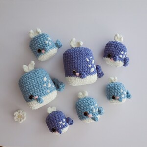 May include: A set of seven crocheted whale plushies in shades of blue and white. The plushies are different sizes and have white accents on their bellies.