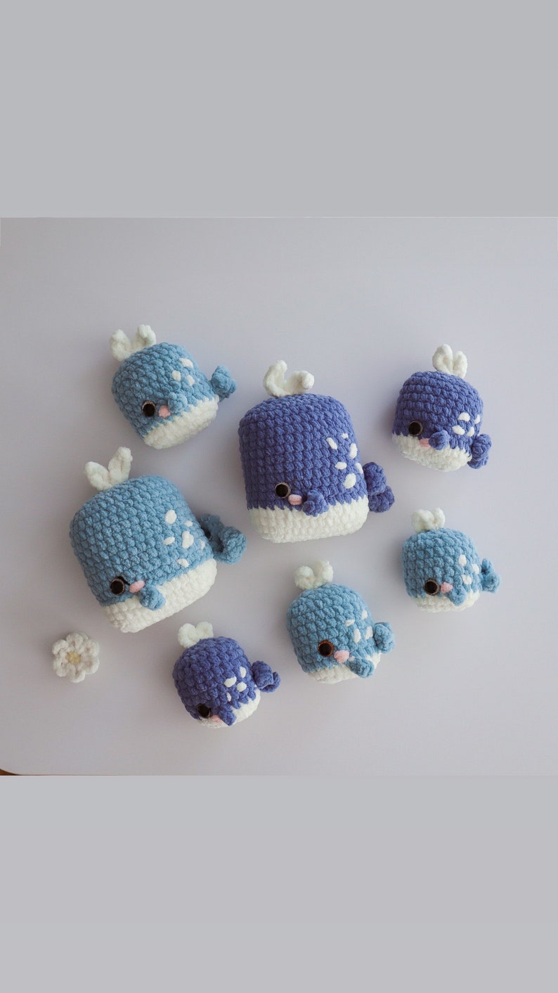 May include: A set of seven crocheted whale plushies in shades of blue and white. The plushies are different sizes and have white accents on their bellies.