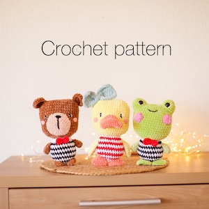 May include: Crochet pattern for a brown bear, yellow duck, and green frog. Each plush toy is wearing a black and white striped outfit with a red bow tie.