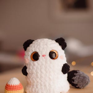May include: White crocheted ghost plush toy with black ears and tail, holding a crocheted candy corn.