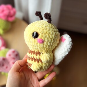 May include: A handmade yellow and brown plush bee with black eyes, pink cheeks, and white wings. The bee has brown antennae and a striped abdomen. The plush toy is soft and cuddly, perfect for children or as a decorative item.