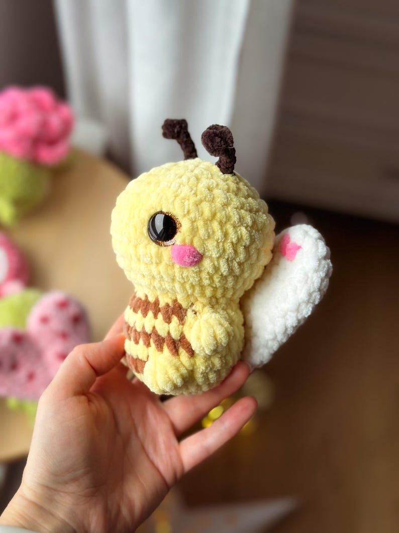 May include: A handmade yellow and brown plush bee with black eyes, pink cheeks, and white wings. The bee has brown antennae and a striped abdomen. The plush toy is soft and cuddly, perfect for children or as a decorative item.