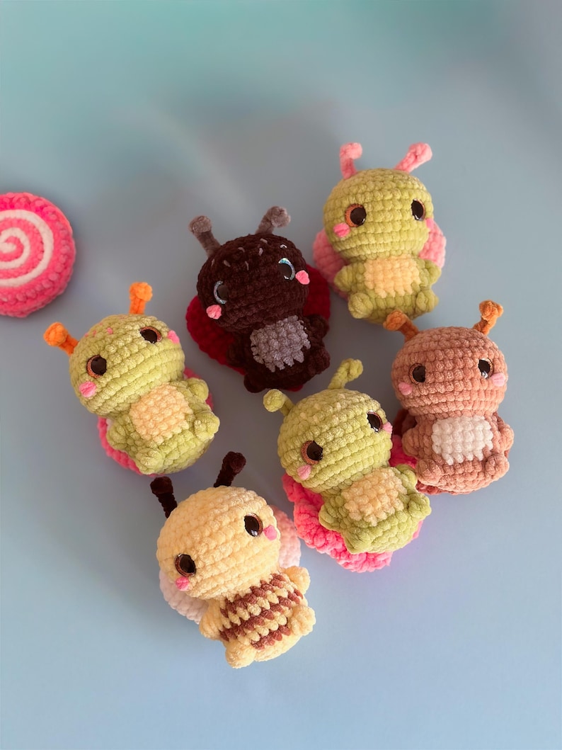May include: A collection of handmade crochet insect toys in various colors, including yellow, green, brown, and peach. Each toy features large eyes, antennae, and wings. A pink and white spiral-shaped crochet item is also present.
