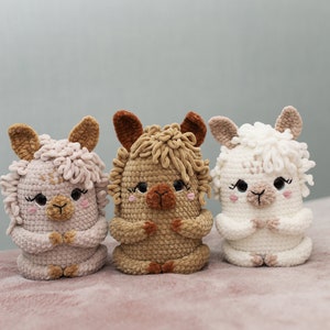 May include: Three handmade crochet alpaca dolls in soft pastel colors. The alpaca dolls are in shades of pink, tan, and white, each with detailed features like ears, eyes, and a fluffy mane. They are sitting upright with their hands clasped.