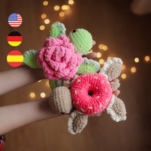 Puede incluir: Dos juguetes de tortuga de crochet. Uno es rosa y blanco con una concha en forma de donut. El otro es verde y blanco con una flor rosa en la espalda.