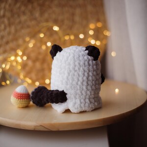 May include: A white crocheted ghost with black ears and a black tail. The ghost is holding a candy corn-shaped object in its hand.