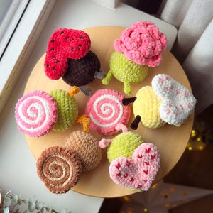 May include: A collection of colorful, handmade crochet food items, including a strawberry, cupcake, and various fruit-shaped designs. The items are arranged on a wooden surface, showcasing a variety of textures and vibrant colors, perfect for a playful aesthetic.