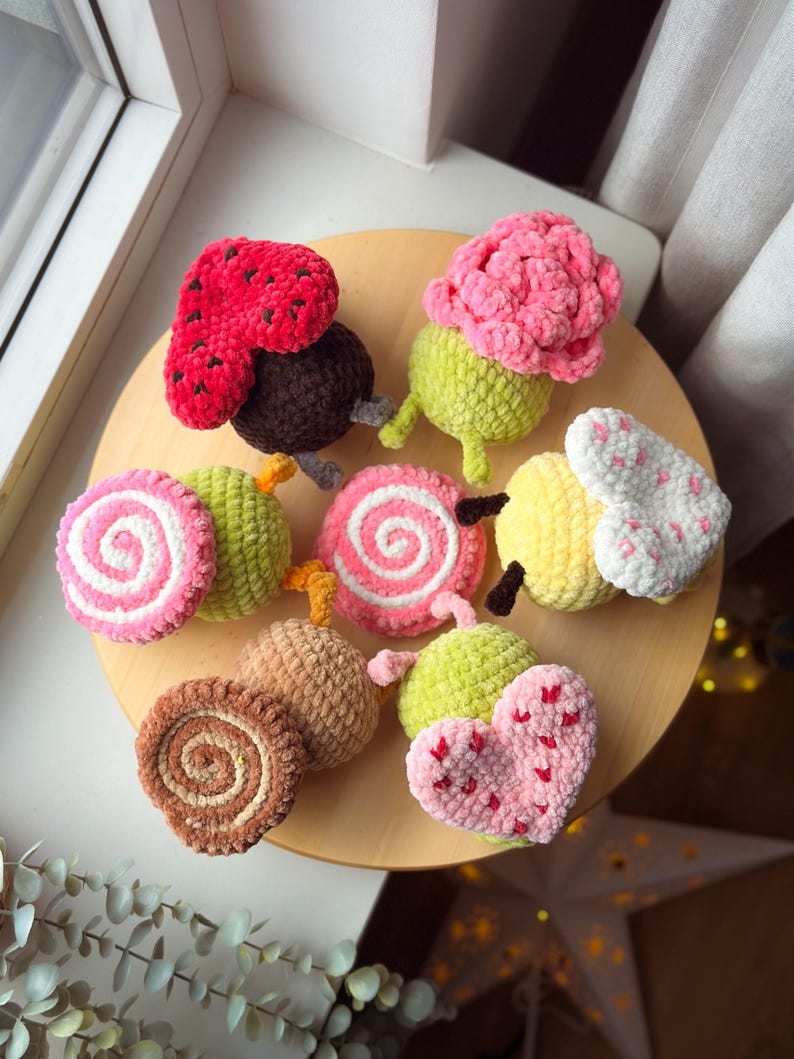 May include: A collection of colorful, handmade crochet food items, including a strawberry, cupcake, and various fruit-shaped designs. The items are arranged on a wooden surface, showcasing a variety of textures and vibrant colors, perfect for a playful aesthetic.