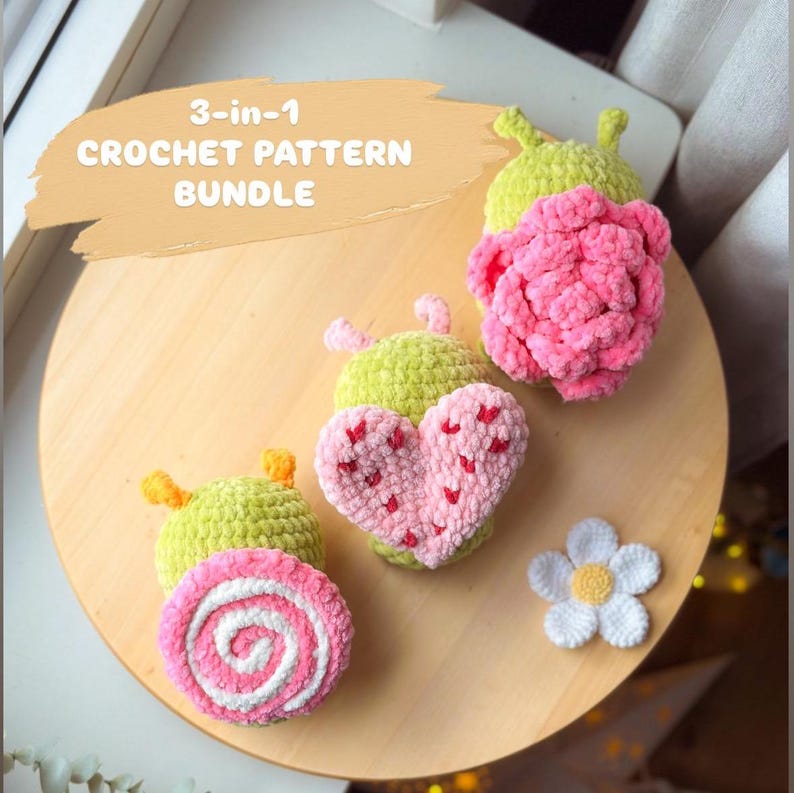 May include: A collection of handmade crochet items, including a pink heart with red accents, a pink and white swirl, a pink flower, and two green caterpillar-like shapes. The text "3-in-1 CROCHET PATTERN BUNDLE" is displayed on a tan background.